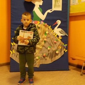 Korytarz w budynku szkoły w Zawadowie. Chłopiec stoi, trzyma książkę. W tle dekoracja - Pani Wiosna